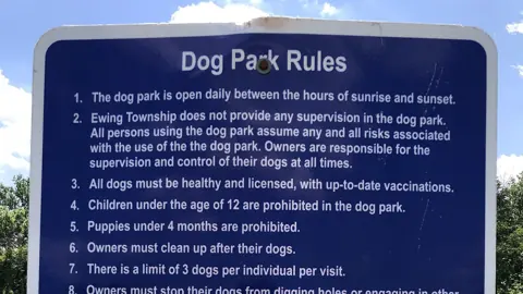 A posted list of dog park rules on a sign by a fence